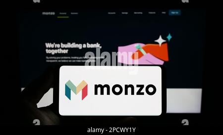 Personne tenant un smartphone avec le logo de la société bancaire britannique Monzo Bank Limited à l'écran devant le site Web. Mise au point sur l'affichage du téléphone. Banque D'Images