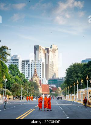 Phnom Penh, Cambodge-23 décembre 2023: Vêtu de robes traditionnelles d'orange, des moines, beaucoup portant des masques de visage, flânez devant le Parc du Palais Royal, sur un large ro Banque D'Images
