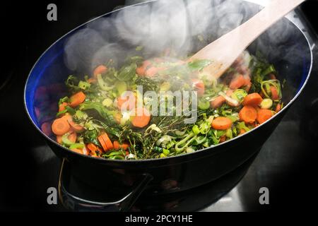 Cuire à la vapeur des légumes et des herbes dans une casserole sur le dessus de la cuisinière noire, les ingrédients pour une soupe comme les carottes, le céleri, le poireau, le thym et les feuilles de Laurier, copie s. Banque D'Images