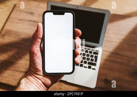 Maquette de smartphone, homme tenant le téléphone mobile avec écran blanc vierge sur ordinateur portable, mise au point sélective Banque D'Images