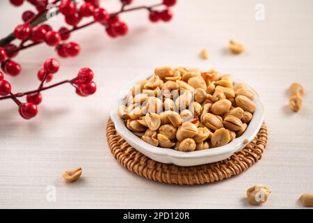 Grains de cacahuètes aromatisés épicés dans un bol sur fond de table blanc. Banque D'Images