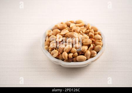 Grains de cacahuètes aromatisés épicés dans un bol sur fond de table blanc. Banque D'Images