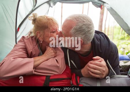 Couple senior romantique s'embrassant à la bouche tout en étant allongé dans la tente pendant le camping en forêt Banque D'Images