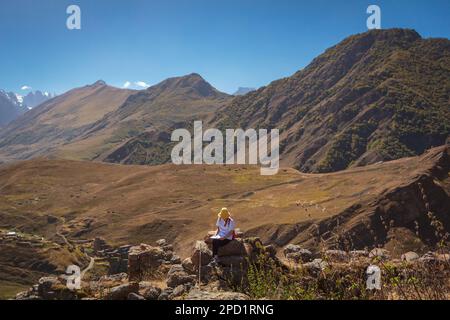 Une jeune fille touristique s'assoit sur une pierre dans les montagnes et regarde la carte de l'itinéraire pour un voyage plus long. Banque D'Images