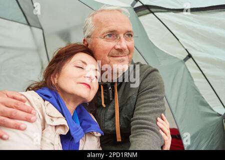 Homme senior attentionné qui embrasse une femme en s'asseyant dans une tente de camping pendant les vacances Banque D'Images
