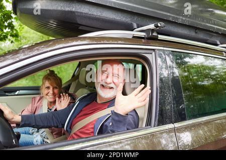 Portrait d'un homme et d'une femme âgés joyeux qui agite en voiture lors d'un voyage en voiture Banque D'Images