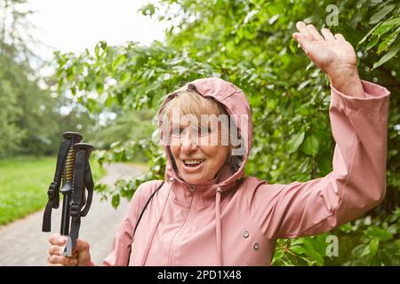 Bonne femme âgée en veste tenant des bâtons de randonnée tout en agitant la main pendant les vacances Banque D'Images