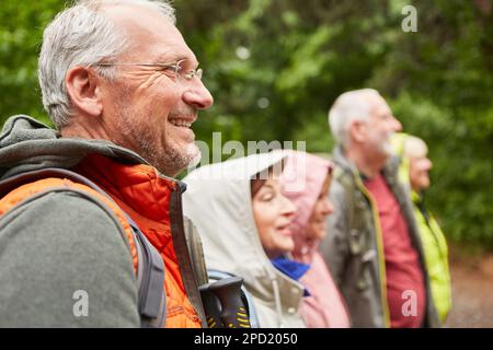 Homme senior souriant en randonnée avec des amis hommes et femmes dans la forêt pendant les vacances Banque D'Images