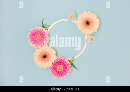 Cadre rond composé de feuilles vertes, d'alstroemeria et de fleurs de gerbera sur fond bleu. Banque D'Images