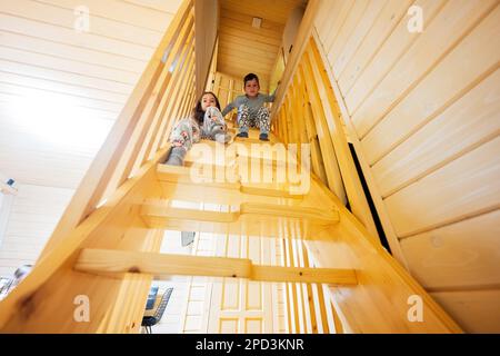 Frère avec soeur en pajama s'asseoir sur les escaliers dans confortable cabane en bois minuscule. La vie à la campagne. Banque D'Images