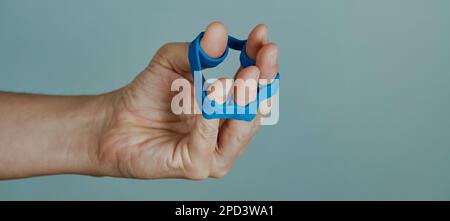 gros plan d'un homme utilisant une bande élastique pour exercer ses doigts sur un fond gris pâle, dans un format panoramique à utiliser comme bannière web ou en-tête Banque D'Images