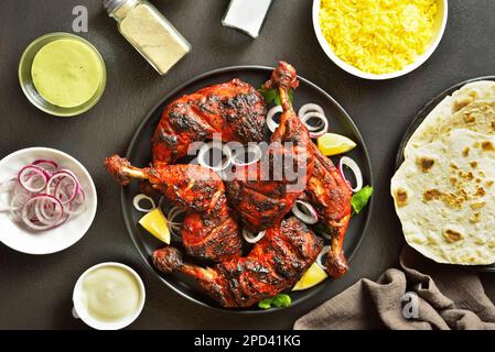Poulet tandoori de style indien sur plaque sur fond de pierre sombre. Cuisses de poulet marinées au yaourt et aux épices. Vue de dessus, plan d'agencement Banque D'Images