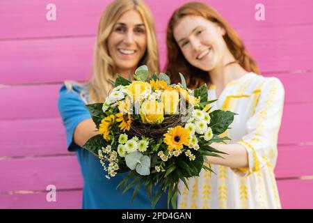 La mère et la fille souriantes présentent un bouquet de fleurs printanières devant un fond rose en bois Banque D'Images