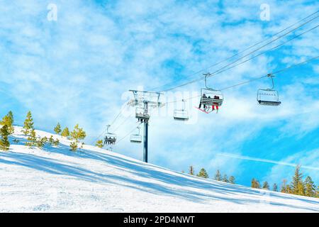 Le télésiège s'élève sur une pente enneigée, au ciel bleu. Les skieurs et les snowboardeurs peuvent être vus en profitant de l'ascenseur, en Banque D'Images