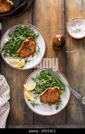 Côtelettes de porc cuites à l'ail servies avec une salade d'arugula sur une assiette Banque D'Images