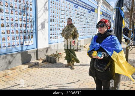 Kiev, Ukraine. 14th mars 2023. Une femme drapée d'un drapeau ukrainien tient des lampes près du mur de la mémoire. La Journée des volontaires a été célébrée au mur de la mémoire de ceux qui sont morts pour l'Ukraine, une commémoration des soldats morts dans la guerre russo-ukrainienne. "Grâce à leur courage et à leur dévouement aux intérêts nationaux, nous avons réussi à arrêter le pays agresseur, à mobiliser les forces à l'arrière et à armer l'armée ukrainienne". Crédit : SOPA Images Limited/Alamy Live News Banque D'Images
