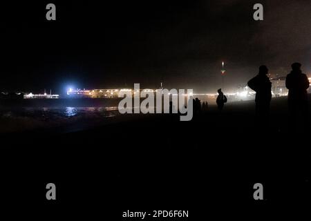 Les gens se rassemblent sur Brighton Beach le soir, silhoueté par le Palace Pier - Brighton & Hove, East Sussex, Royaume-Uni Banque D'Images