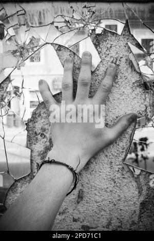 Un miroir cassé sur un mur industriel en béton touché par les mains humaines Banque D'Images