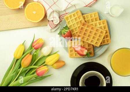 Gaufres maison fraîchement préparées sur une assiette. Gaufres maison avec fraises. Tulipes et gaufres au café. Vue latérale Banque D'Images