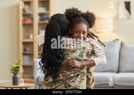 Petite fille souriant à l'appareil photo tout en embrassant sa mère pendant son retour à la maison Banque D'Images