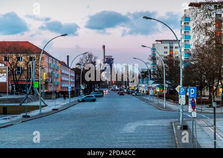 Section centrale de Lindenallee (anciennement Leninallee) à Eisenhüttenstadt avec séquence rythmique de bâtiments de haute hauteur avec des toits et des magasins en saillie. Au bout de l'avenue, vue sur le grand haut-fourneau. L'ancienne aciérie EKO (Eisenhütten Kombinat Ost) d'ArcelorMittal à Eisenhüttenstadt, en Allemagne Banque D'Images