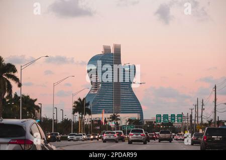 Architecture en forme de guitare de l'hôtel Hard Rock depuis une avenue avec des voitures. Avion à l'arrière du bâtiment pendant un coucher de soleil à Hollywood, Floride Banque D'Images