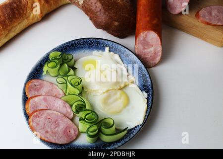 petit déjeuner saucisse jambon œufs brouillés salade concombre sur une assiette vue d'en haut sur un fond blanc. Petit déjeuner à l'hôtel nourriture saine. Banque D'Images