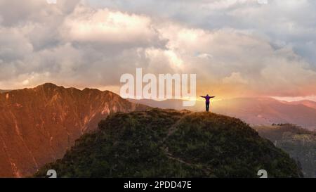 Jeune femme solitaire vue de derrière avec les bras étendus sur le sommet d'une montagne sur fond nuageux coucher de soleil Banque D'Images