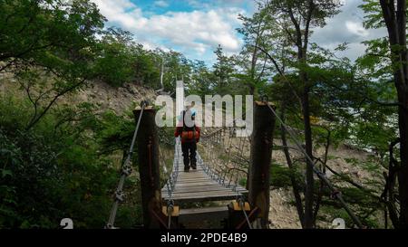 Jeune touriste avec sac à dos vu de l'arrière traversant un pont suspendu entouré d'arbres par une journée ensoleillée Banque D'Images