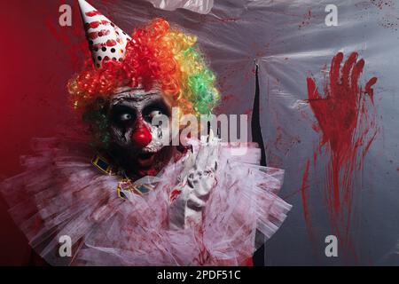 Un clown terrifiant près d'un film de plastique coloré par le sang. Costume de fête d'Halloween Banque D'Images