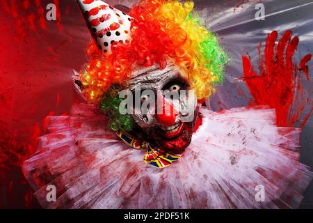 Un clown terrifiant près d'un film de plastique coloré par le sang. Costume de fête d'Halloween Banque D'Images