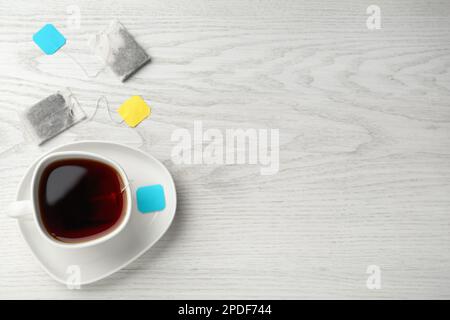 Sachets de thé dans une tasse en céramique d'eau chaude sur une table en bois blanc, plat. Espace pour le texte Banque D'Images