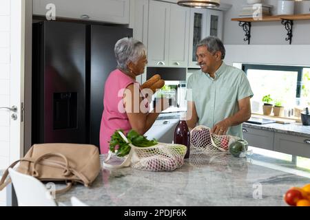 Un couple biracial senior parlant en dépassant les produits d'épicerie sur le comptoir de la cuisine à la maison, espace de copie Banque D'Images