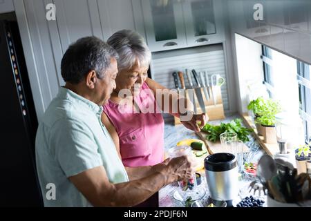 Vue en grand angle du couple biracial senior qui fait des smoothies de fruits sur le comptoir de cuisine à la maison Banque D'Images