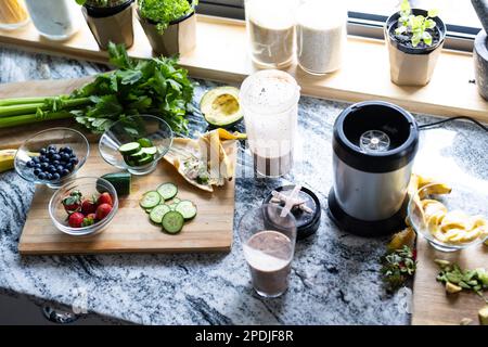 Vue en grand angle du smoothie dans le verre à boire et du blender avec fruits et herbes sur le plan de travail de la cuisine Banque D'Images