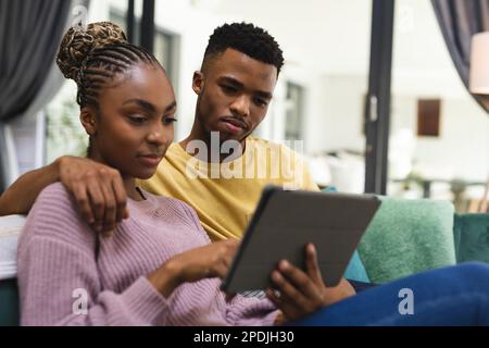Heureux couple afro-américain assis sur un canapé et utilisant une tablette Banque D'Images