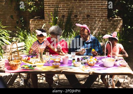 Joyeux grand-parents et petits-enfants afro-américains colorant les œufs de pâques dans le jardin Banque D'Images