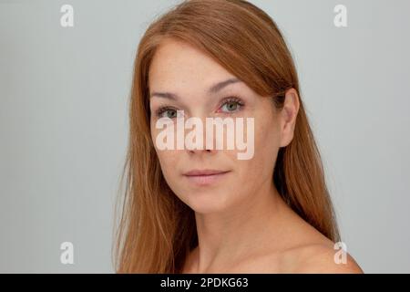 Portrait d'une femme d'âge moyen aux cheveux rougeâtres et au calme regarder l'appareil photo sur fond gris Banque D'Images