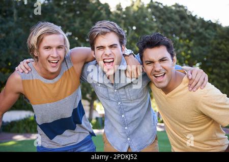 Amis pour la vie. Portrait de trois amis qui applaudissent debout les uns autour des autres dans un parc. Banque D'Images