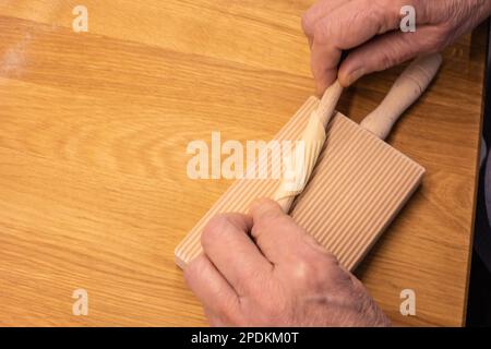 Production de pâtes maison - nouilles italiennes (Tortiglioni) à faire soi-même - gros plan des mains roulant la pâte pour préparer des Tortiglioni faits maison Banque D'Images