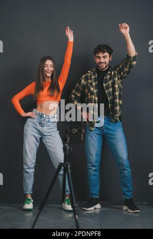 Un couple enthousiaste enregistre un clip vidéo de danse pour les médias sociaux à l'aide d'un téléphone portable sur trépied, faisant des mouvements de danse sur fond de mur noir. Défi Internet Banque D'Images