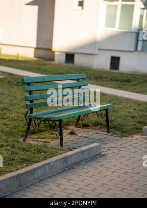 Un banc de parc vert se trouve sur la pelouse en face d'une maison de banlieue. Banque D'Images