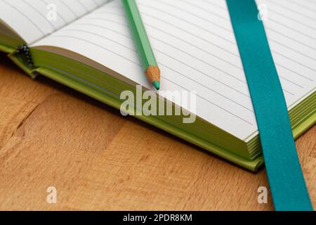 Un carnet doublé avec un crayon vert. Prêt à prendre des notes, à esquisser des idées et à rédiger des plans. Crayon et papier à portée de main. Banque D'Images