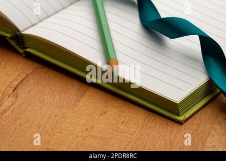 Un carnet doublé avec un crayon vert. Prêt à prendre des notes, à esquisser des idées et à rédiger des plans. Crayon et papier à portée de main. Banque D'Images