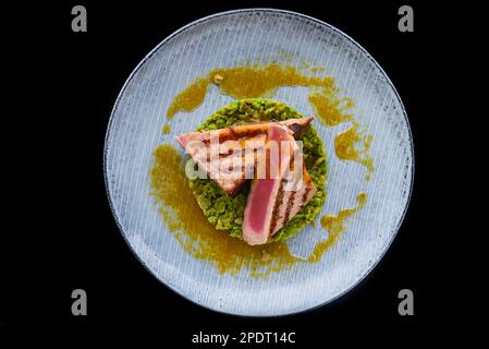 Beefsteak moyen rare avec du sang servi avec des petits pois isolés sur fond noir vue latérale Banque D'Images