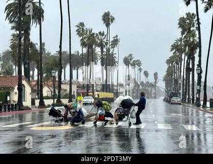 Santa Barbara, Californie, États-Unis. 14th mars 2023. Sur 14 mars 2023, une grande partie du comté de Santa Barbara a été soumise à des ordres d'évacuation obligatoires pendant une tempête atmosphérique qui a fait tomber la pluie sans pause pendant douze heures. Ici, un homme qui dormait habituellement dans les rues ou sur les plages et les parcs de Santa Barbara et qui n'a pas d'endroit où aller a dû se déplacer pour éviter les zones inondées d'herbe ou de sable, et a été laissé pour déplacer tous ses effets personnels sous la pluie verglaçante: il a fait un train de plusieurs charrettes et même une poussette pour bébé, et a trouvé refuge sous une dizaine de la ville avait mis en place pour les personnes ayant besoin de couverture sur la promenade latérale. (CRED Banque D'Images