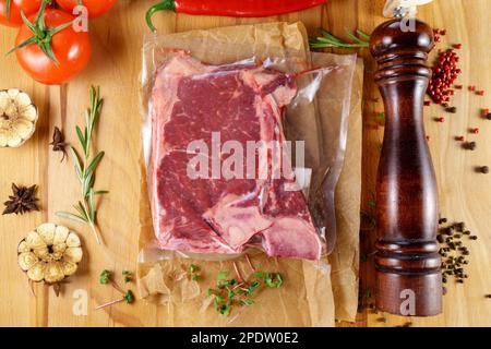 Viande emballée à l'aspirateur, sur une planche de bois, steak. Vue de dessus. Diverses épices Banque D'Images