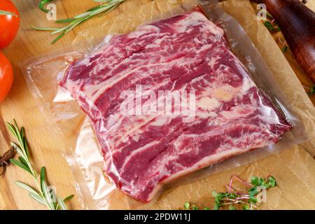 Viande emballée à l'aspirateur, sur une planche de bois, steak. Vue de dessus. Diverses épices Banque D'Images