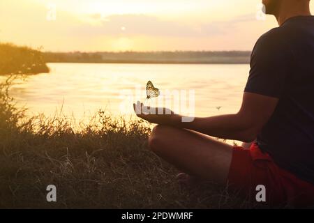 Homme méditant près de la rivière au coucher du soleil, à proximité. Espace pour le texte Banque D'Images