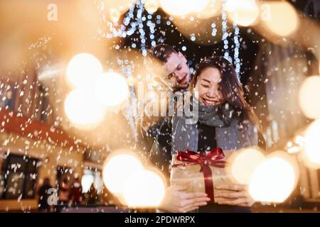 Contient une boîte cadeau. Heureux couple multiracial ensemble en plein air dans la ville célébrant le nouvel an Banque D'Images